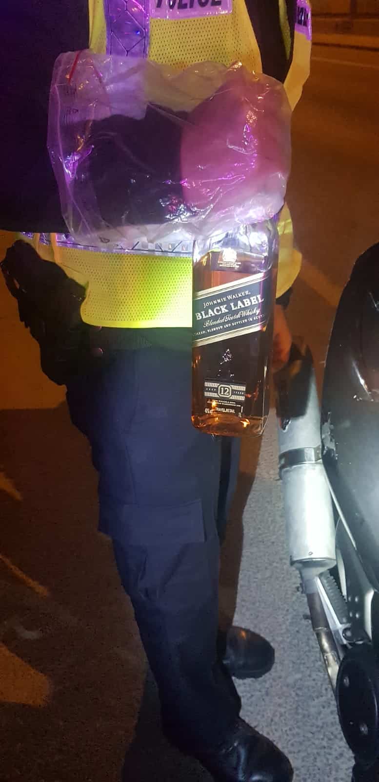 שוטר מחזיק את בקבוק הוויסקי שנתפס בתא הכיסא (צילום: דוברות המשטרה)